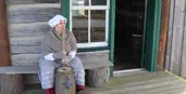 Lady dressed in early settler clothing with a bonnet on churning butter.